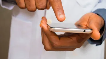 Image shows two hands holding a smartphone. The person's is wearing a labcoat.