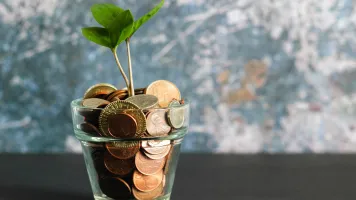Glass of coins with a sprouting plant growing out of it