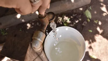 A close-up of water being collected in a cup from a tap, taken from above, in Paraguay