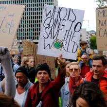 People in a crowd holding signs above their heads with words and pictures on them. They appear to be marching and shouting. 