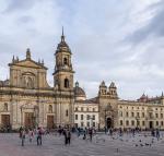 A stone church with two towers in the background of a plaza with people and birds in the foreground.