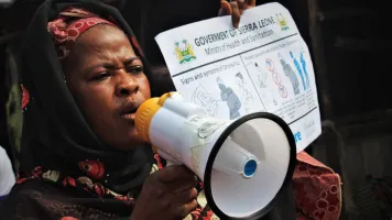 Kaddy Mansaray providing COVID prevention information at the market with a poster and megaphone. Credit: Trocaire