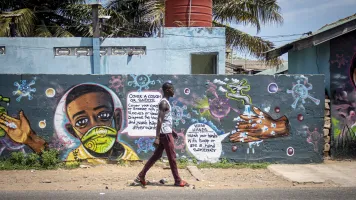 Man in Ghana walking in front of a wall of COVID-related graffiti