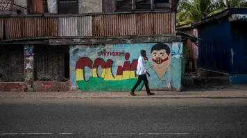 Man walking across an empty street in Accra, Ghana, with "COVID-19" graffitied on the wall