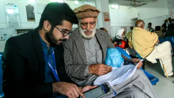 Two men sitting in a waiting room looking at a tablet