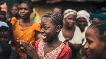 A girl smiling and clapping amidst a group of women. 