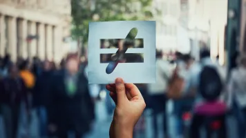 Inequality sign held in front of crowd.