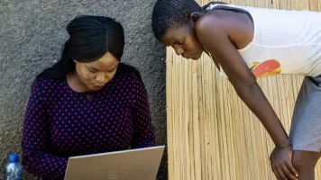 Two women look at a computer.