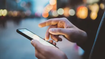 Two hands holding a mobile phone against a city-scape background.