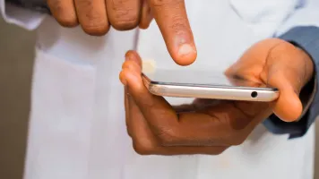 Image shows two hands holding a smartphone. The person's is wearing a lab coat.