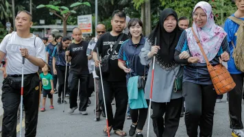 People with vision impairments walk together with a sighted person guiding at the Perdana Lake in Kuala Lumpur, Malaysia. Credit: Lens Hitam/Shutterstock