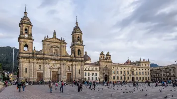 A stone church with two towers in the background of a plaza with people and birds in the foreground.