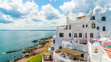 Bright white buildings on a cliff above the sea with dramatic clouds in the background.