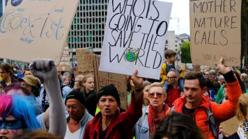 People in a crowd holding signs above their heads with words and pictures on them. They appear to be marching and shouting. 