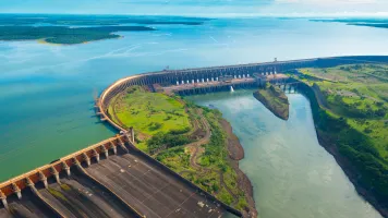 Aerial view of a dam with rushing blue-green water on both sides surrounded by greenery.