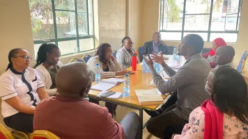 Participants in learning exchange from Ministries of Health in Kenya and Zanzibar sitting around a table holding debrief meeting