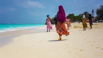 Women wearing colourful traditional clothes walking on Nungwi beach on the island of Zanzibar, Tanzania