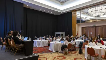 Attendees sit at six round tables in front of a panel of four speakers at the workshop to discuss progress on the Power of Data High Impact Initiative, at Day Zero of Festival de Datos