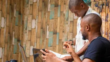 Two people collaborating, looking at two laptops and a smartphone