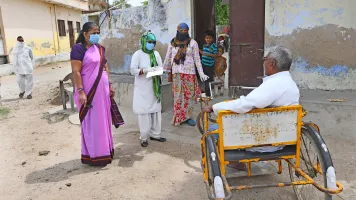Beawar, India-April 20,2020: Anganwadi workers wearing protective face mask interacts with a disabled man during a door-to-door survey