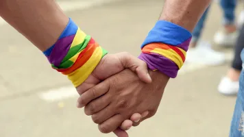 pareja gay cogidos de la mano paseando. Primer plano de pareja de la comunidad LGBT. Bandera del arco iris