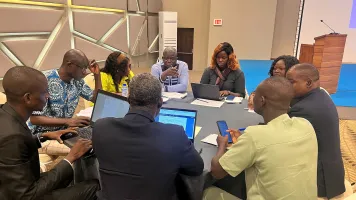 A group of nine people sitting around a circular table and collaborating at the Managing environmental data and climate statistics event in Togo
