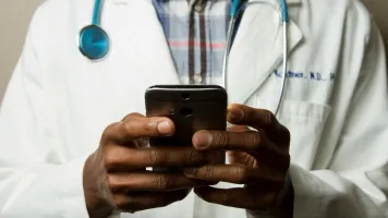 Doctor holding mobile phone. Photo: National Cancer Institute / Unsplash 