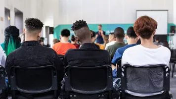 Three students in the back row of a class in school. Photo by Sam Bailey, via Unsplash