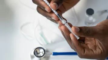 A close up of a medic's hands holding a syringe, with a stethoscope in the background. Photo by Nappy, via Unsplash
