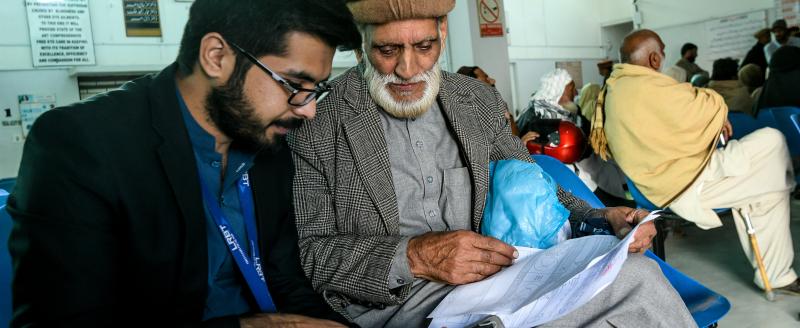 Two men sitting in a waiting room looking at a tablet