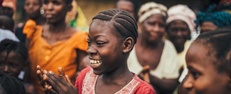 A girl smiling and clapping amidst a group of women.