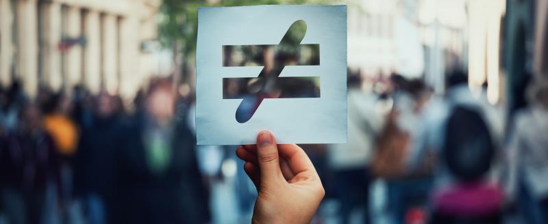 Inequality sign held in front of crowd.