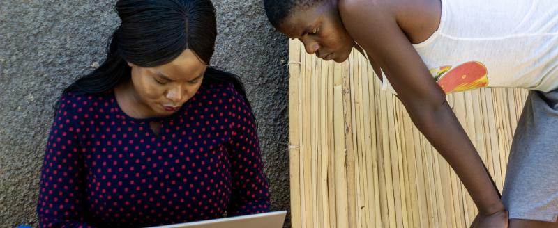 Two women look at a computer.