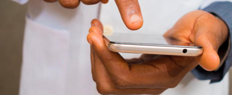 Image shows two hands holding a smartphone. The person's is wearing a labcoat.