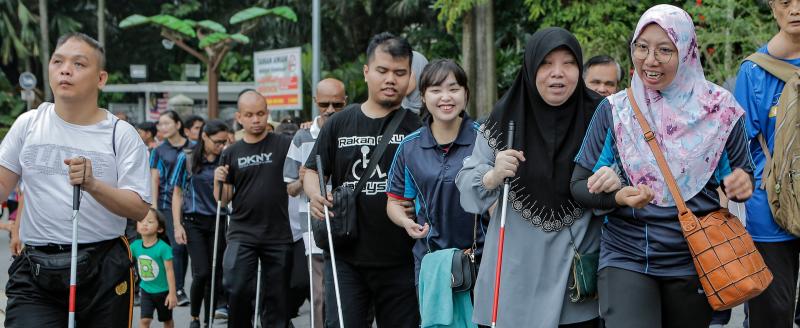 People with vision impairments walk together with a sighted person guiding at the Perdana Lake in Kuala Lumpur, Malaysia. Credit: Lens Hitam/Shutterstock