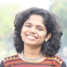 A brown-skinned woman with curly black hair in a striped shirt smiles facing the camera.