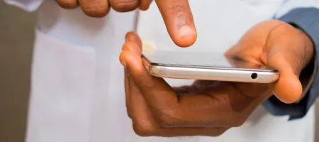 Image shows two hands holding a smartphone. The person's is wearing a labcoat.