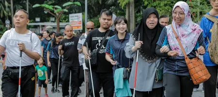 People with vision impairments walk together with a sighted person guiding at the Perdana Lake in Kuala Lumpur, Malaysia. Credit: Lens Hitam/Shutterstock