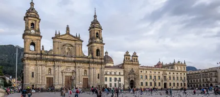 A stone church with two towers in the background of a plaza with people and birds in the foreground.