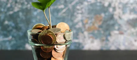 Glass of coins with a sprouting plant growing out of it