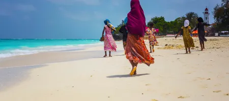 Women wearing colourful traditional clothes walking on Nungwi beach on the island of Zanzibar, Tanzania
