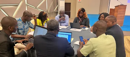 A group of nine people sitting around a circular table and collaborating at the Managing environmental data and climate statistics event in Togo