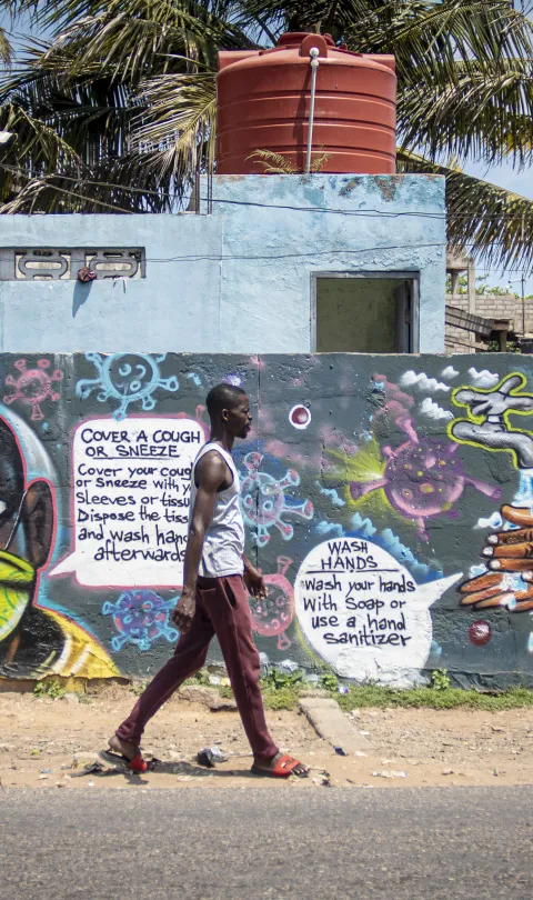 Man in Ghana walking in front of a wall of COVID-related graffiti