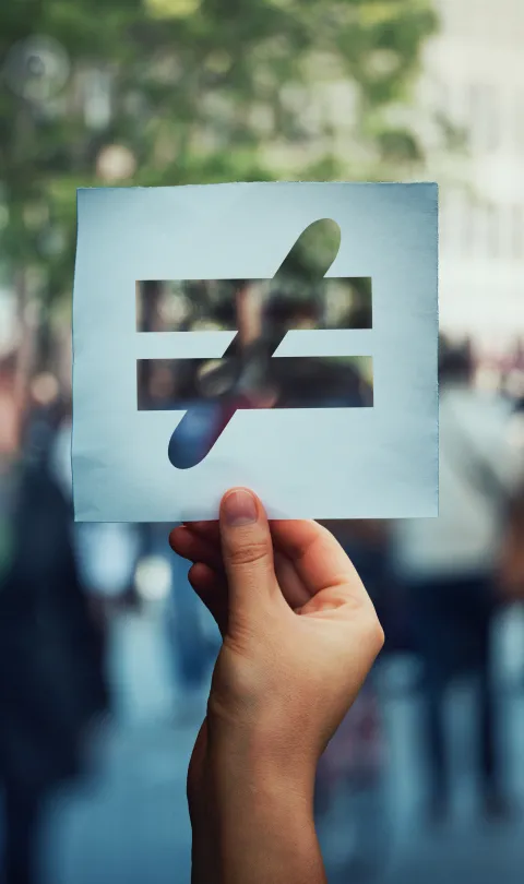 Inequality sign held in front of crowd.