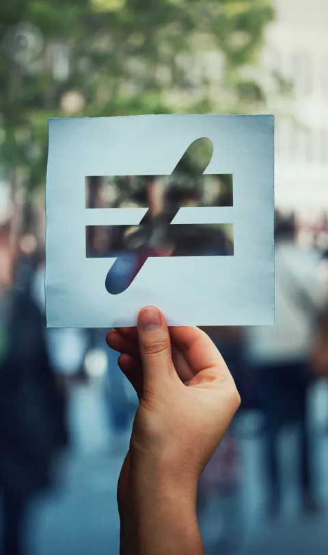 Inequality sign held in front of a crowd.