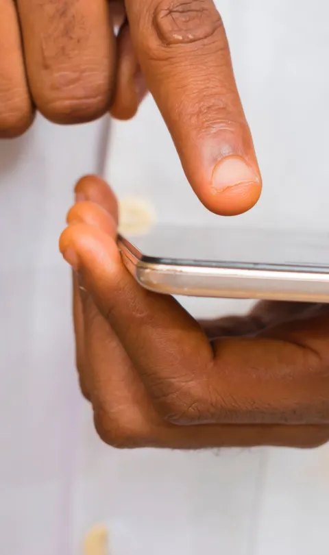 Image shows two hands holding a smartphone. The person's is wearing a lab coat.