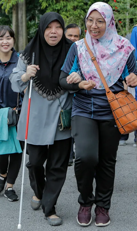 People with vision impairments walk together with a sighted person guiding at the Perdana Lake in Kuala Lumpur, Malaysia. Credit: Lens Hitam/Shutterstock