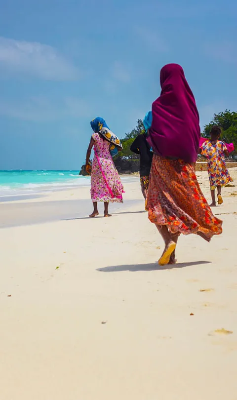 Women wearing colourful traditional clothes walking on Nungwi beach on the island of Zanzibar, Tanzania