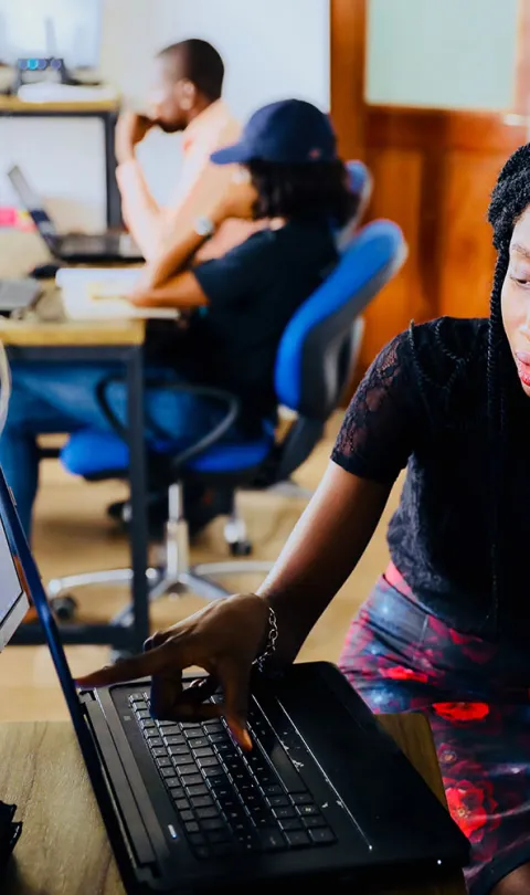 Two people sitting in front of a desktop computer and working together. One person is pointing at the screen. Photo by Desola Lanre Ologun, via Unsplash