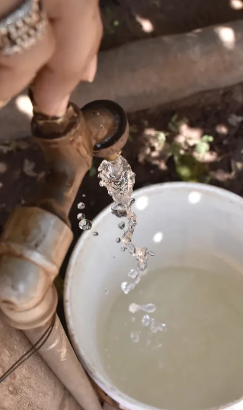 A close-up of water being collected in a cup from a tap, taken from above, in Paraguay